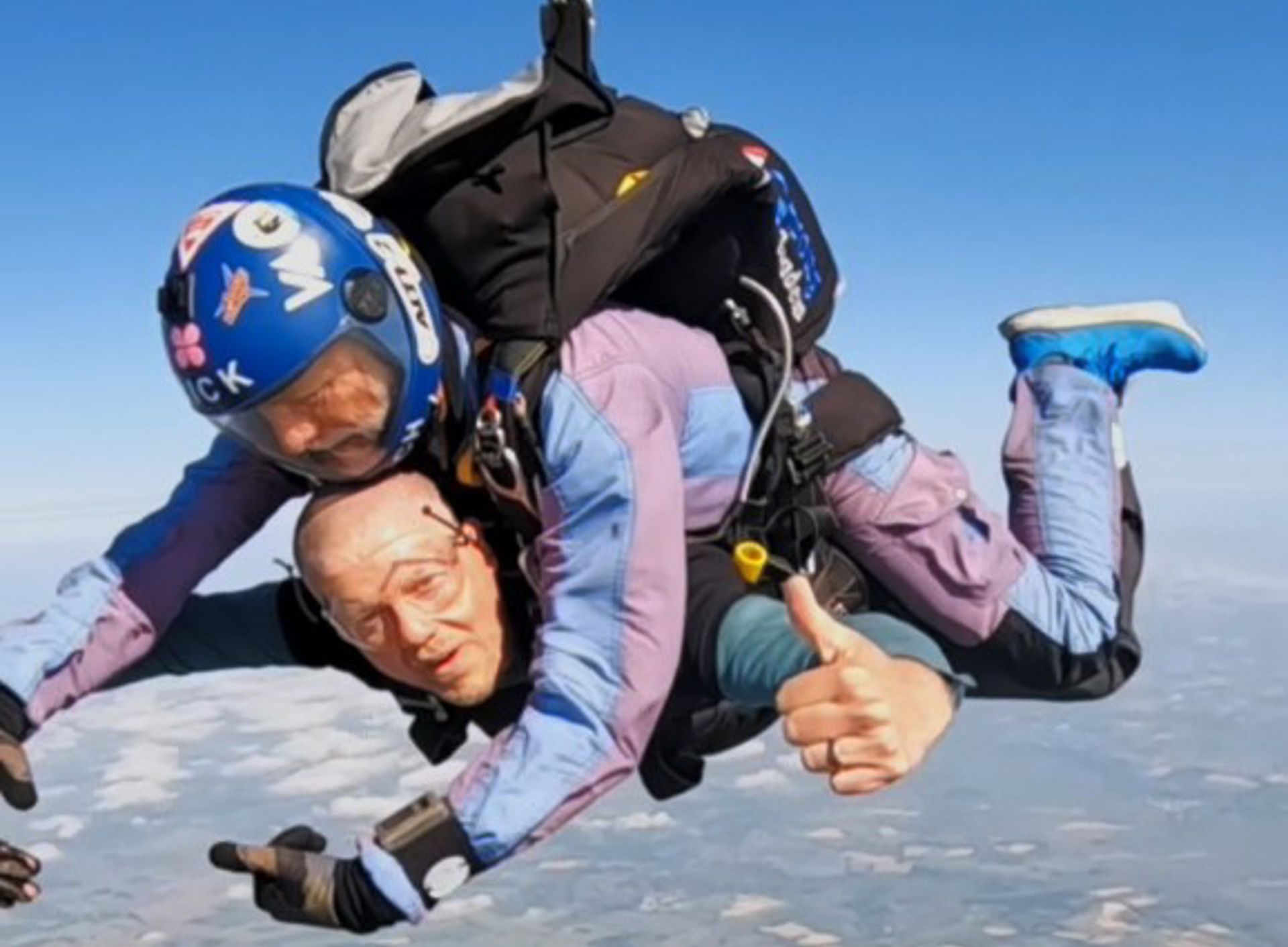 A picture of two men skydiving, one man is looking at the camera giving a thumbs up.